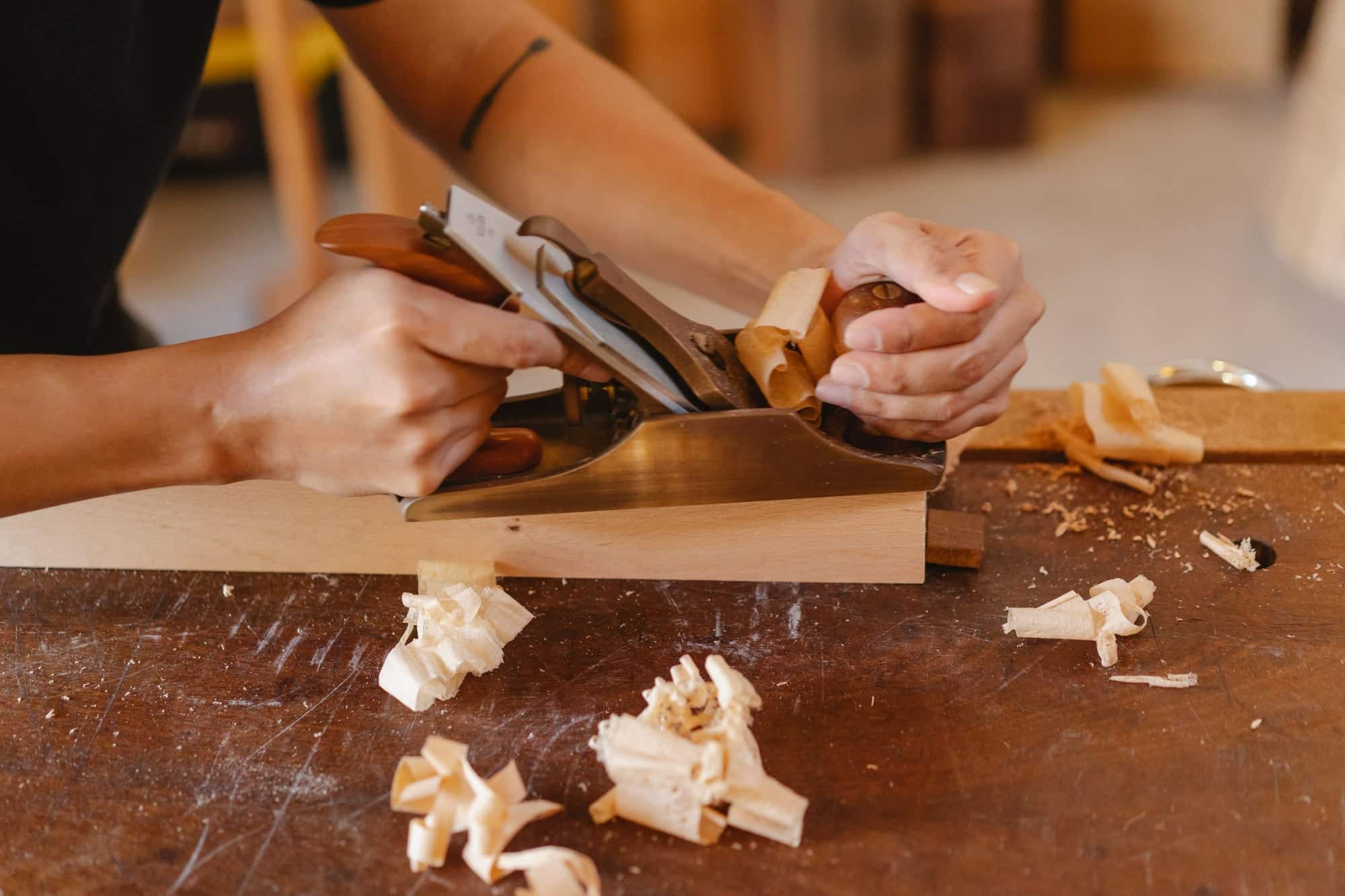 Mains d'un menuisier rabotant une pièce de bois avec un rabot à main sur un établi